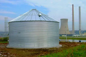 Large silver corrugated steel water tank with a conical roof, located near industrial structures.